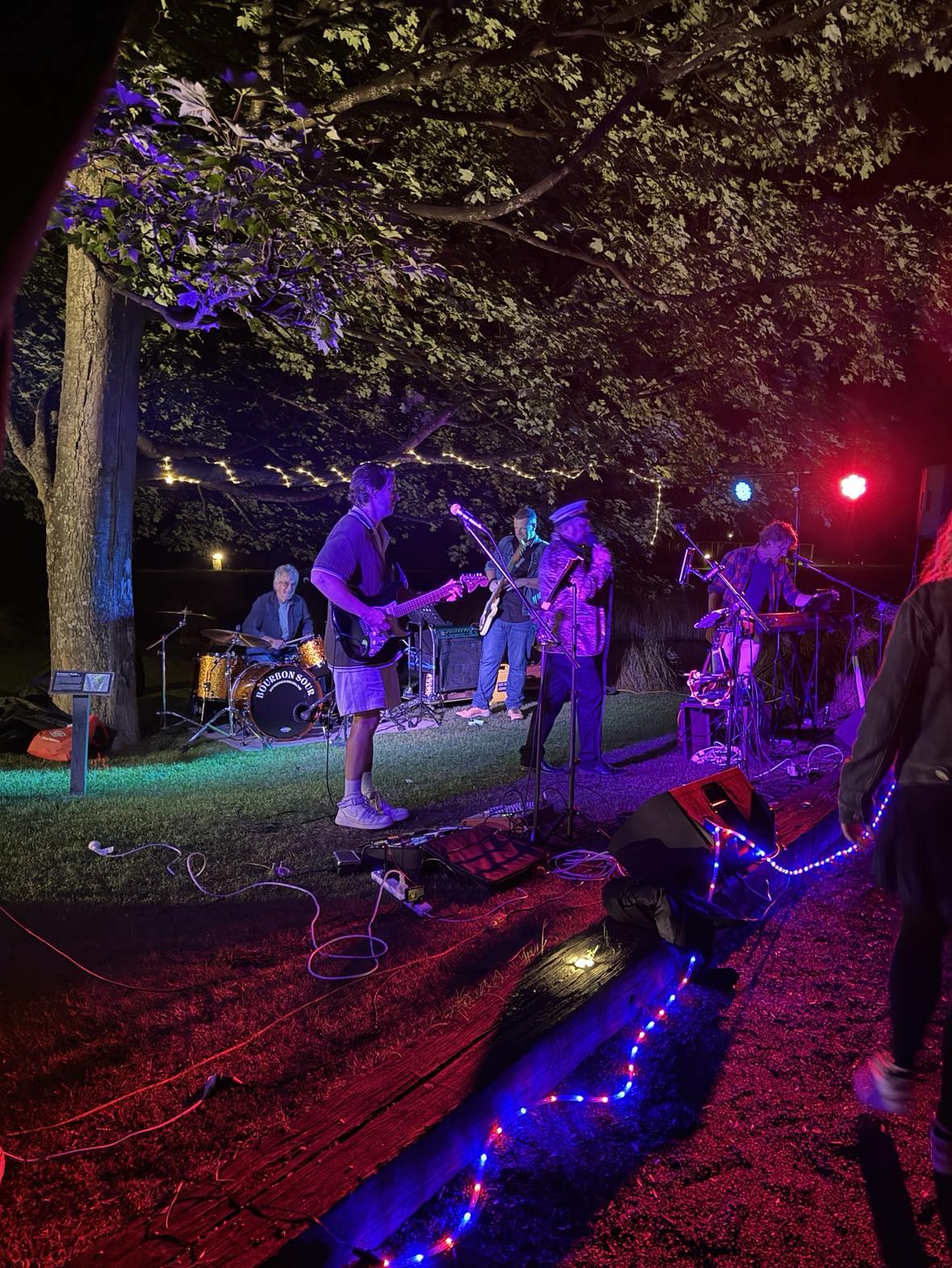 Live outdoor performance by a vibrant rock band under string lights, energizing a crowd at a nighttime event � perfect for weddings, parties, and special occasions in Queenstown and Central Otago.